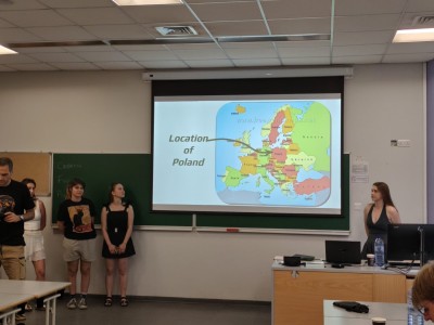 4 studentki stoją w sali lekcyjnej i opisują wyświetlane przez siebie slajdy prezentacji o Polsce.. Kliknij, aby powiększyć zdjęcie.