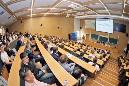 Kadry z inauguracji roku akademickiego w Audytorium Aleksandra Jabłońskiego - kolegium dziekańskie wraz z prorektorką za stołem oraz studenci i nauczyciele oraz administracja siedzący na sali. Kliknij, aby powiększyć zdjęcie.