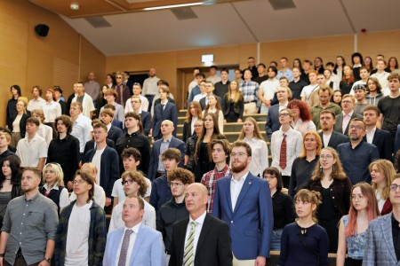 Kadry z inauguracji roku akademickiego w Audytorium Aleksandra Jabłońskiego - kolegium dziekańskie wraz z prorektorką za stołem oraz studenci i nauczyciele oraz administracja siedzący na sali. Kliknij, aby powiększyć zdjęcie.