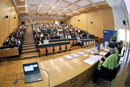 Kadry z inauguracji roku akademickiego w Audytorium Aleksandra Jabłońskiego - kolegium dziekańskie wraz z prorektorką za stołem oraz studenci i nauczyciele oraz administracja siedzący na sali. Kliknij, aby powiększyć zdjęcie.