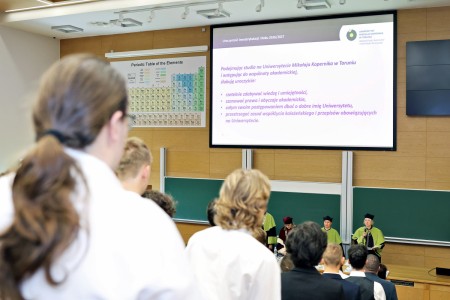 Kadry z inauguracji roku akademickiego w Audytorium Aleksandra Jabłońskiego - kolegium dziekańskie wraz z prorektorką za stołem oraz studenci i nauczyciele oraz administracja siedzący na sali. Kliknij, aby powiększyć zdjęcie.