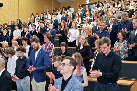 Kadry z inauguracji roku akademickiego w Audytorium Aleksandra Jabłońskiego - kolegium dziekańskie wraz z prorektorką za stołem oraz studenci i nauczyciele oraz administracja siedzący na sali. Kliknij, aby powiększyć zdjęcie.