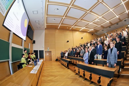 Kadry z inauguracji roku akademickiego w Audytorium Aleksandra Jabłońskiego - kolegium dziekańskie wraz z prorektorką za stołem oraz studenci i nauczyciele oraz administracja siedzący na sali. Kliknij, aby powiększyć zdjęcie.