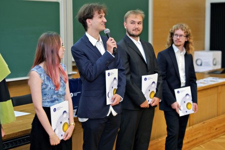 Kadry z inauguracji roku akademickiego w Audytorium Aleksandra Jabłońskiego - kolegium dziekańskie wraz z prorektorką za stołem oraz studenci i nauczyciele oraz administracja siedzący na sali. Kliknij, aby powiększyć zdjęcie.