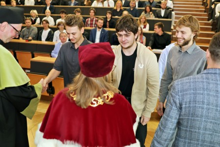 Kadry z inauguracji roku akademickiego w Audytorium Aleksandra Jabłońskiego - kolegium dziekańskie wraz z prorektorką za stołem oraz studenci i nauczyciele oraz administracja siedzący na sali. Kliknij, aby powiększyć zdjęcie.