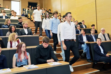 Kadry z inauguracji roku akademickiego w Audytorium Aleksandra Jabłońskiego - kolegium dziekańskie wraz z prorektorką za stołem oraz studenci i nauczyciele oraz administracja siedzący na sali. Kliknij, aby powiększyć zdjęcie.