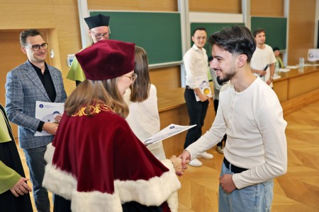 Kadry z inauguracji roku akademickiego w Audytorium Aleksandra Jabłońskiego - kolegium dziekańskie wraz z prorektorką za stołem oraz studenci i nauczyciele oraz administracja siedzący na sali. Kliknij, aby powiększyć zdjęcie.