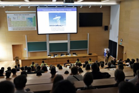 Kadry z inauguracji roku akademickiego w Audytorium Aleksandra Jabłońskiego - kolegium dziekańskie wraz z prorektorką za stołem oraz studenci i nauczyciele oraz administracja siedzący na sali. Kliknij, aby powiększyć zdjęcie.