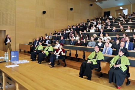 Kadry z inauguracji roku akademickiego w Audytorium Aleksandra Jabłońskiego - kolegium dziekańskie wraz z prorektorką za stołem oraz studenci i nauczyciele oraz administracja siedzący na sali. Kliknij, aby powiększyć zdjęcie.