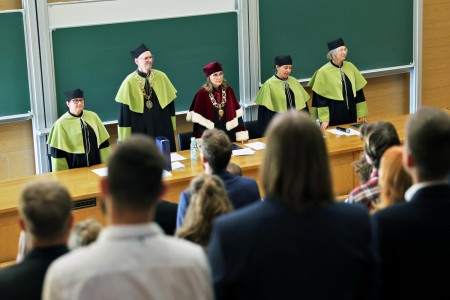 Kadry z inauguracji roku akademickiego w Audytorium Aleksandra Jabłońskiego - kolegium dziekańskie wraz z prorektorką za stołem oraz studenci i nauczyciele oraz administracja siedzący na sali. Kliknij, aby powiększyć zdjęcie.