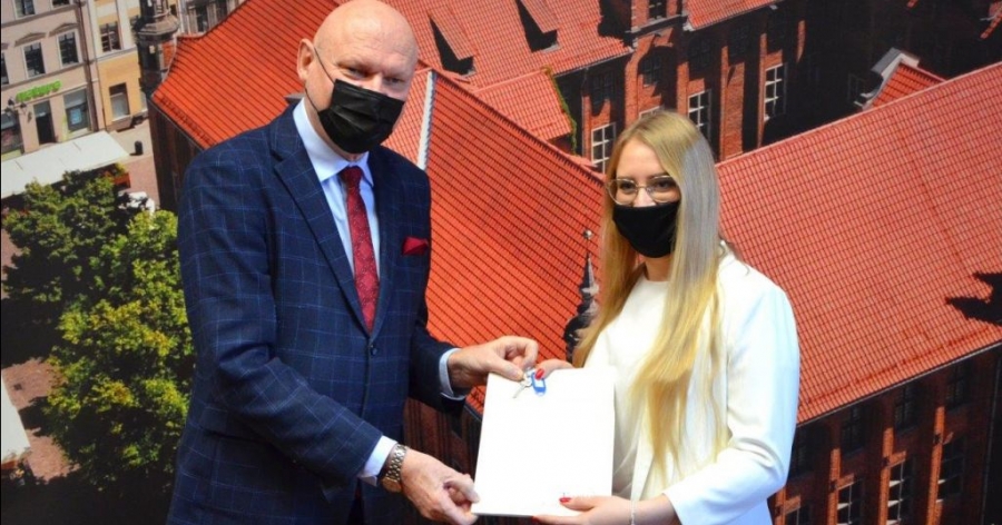 prezydent miasta wręczający klucze absolwentce, w tle zdjęcie toruńskiego ratusza
