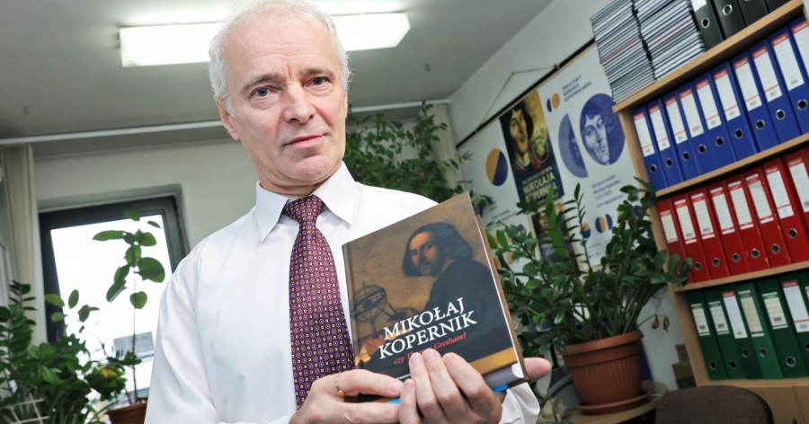 Starszy mężczyzna stoi i trzyma w dłoniach książkę pt. Mikołaj Kopernik czy Thomas Gresham?