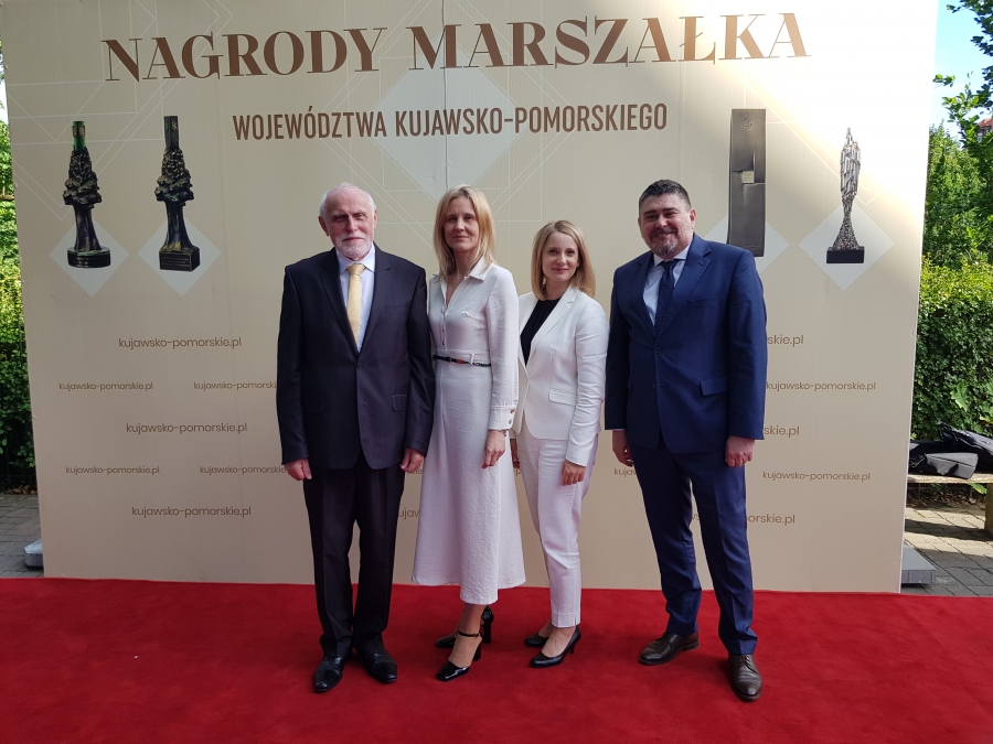 4 osoby (2 mężczyzn i 2 kobiety) stojące na tle ścianki z napisem 