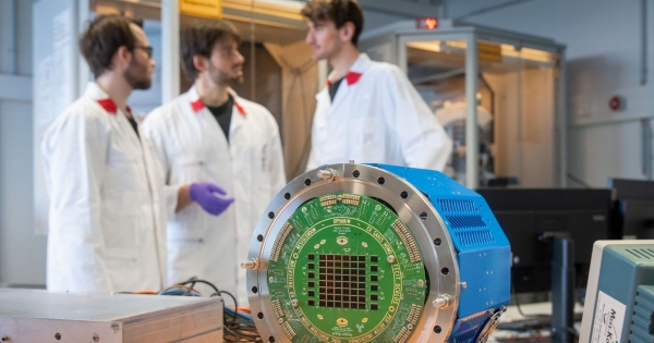 Three scientists stand in a lab. In the foreground you can see a device with colored sensors