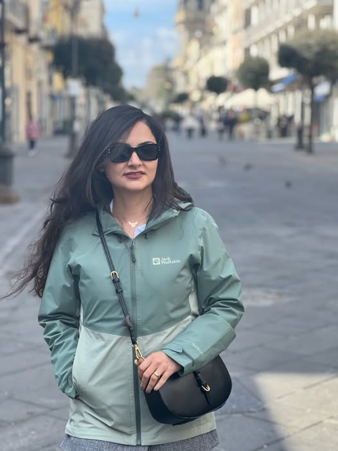 Woman in a green jacket and sunglasses walking down a city street