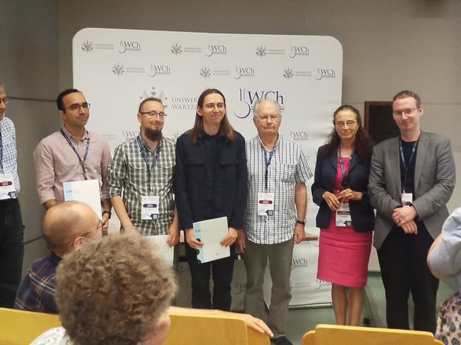 Group of people standing with certificates at an event in front of a University of Warsaw backdrop