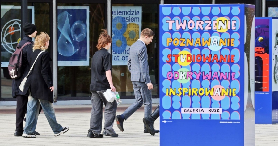 Grupa studentów idzie wzdłuż rektoratu, w centralnym punkcie zdjęcia widać również plakat Galerii Rusz, na której napisano 