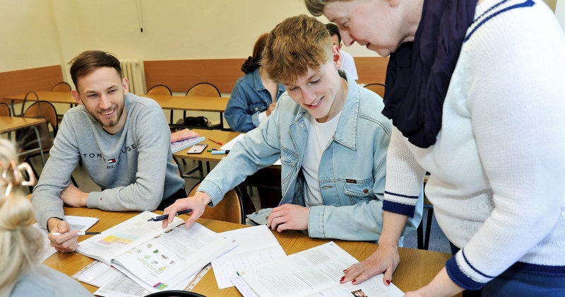 Two students with lecturer are looking at open workbooks