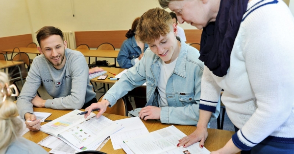 Two students with lecturer are looking at open workbooks