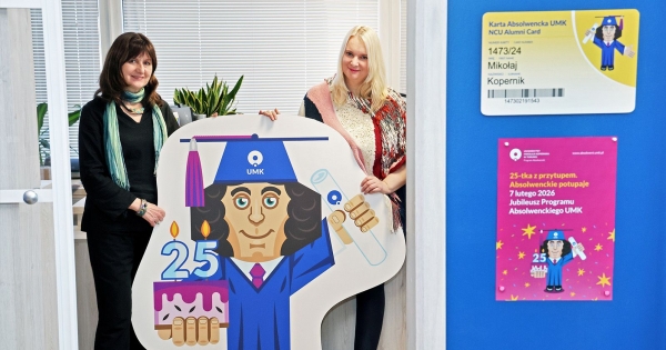 Dwie kobiety stoją. Trzymają wyciętą z tektury postać Mikołaja Kopernika w birecie, trzymającą tort z cyframi 25. To tort z okazji 25 lat działalności Programu Absolwenckiego UMK