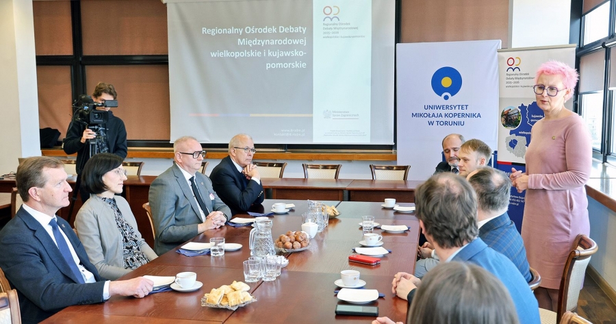 Kobiety i mężczyźni siedzą wokół stołu konferencyjnego, stoi i przemawia dr hab. Magdalena Barwiołek