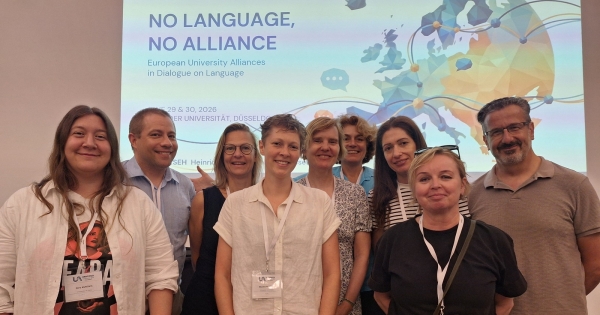 Grupa uczestników konferencji UNIVERSEH 2026 przed ekranem z hasłem ?No Language, No Alliance?.