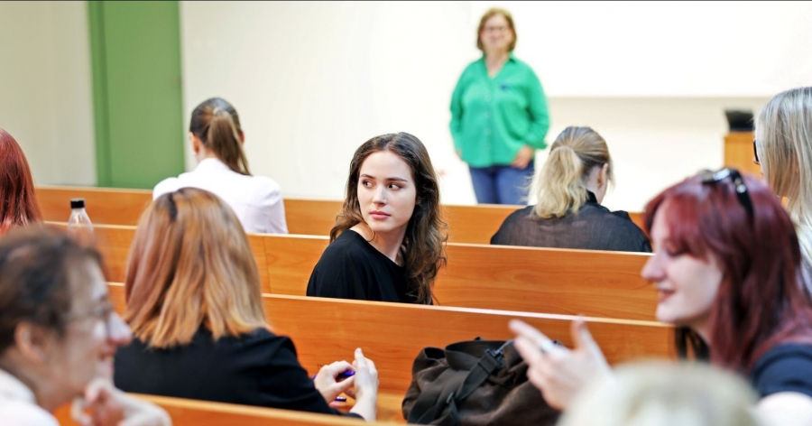 Female students are sitting at desks in a lecture hall; the person in the center of the frame is looking over her shoulder