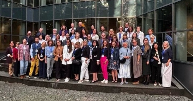 In the foreground, a group of workshop participants stands in 4 rows in front of the Faculty of Law building at Jagiellonian University in Krakow.