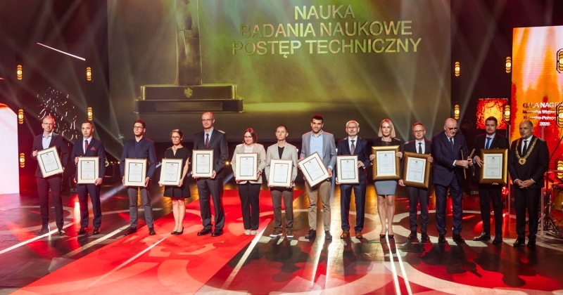 Grupa laureatów stojąca na scenie z oprawionymi w ramy dyplomami podczas Gali Nagród Marszałka Województwa Kujawsko-Pomorskiego w kategorii ?Nauka, badania naukowe, postęp techniczny?.